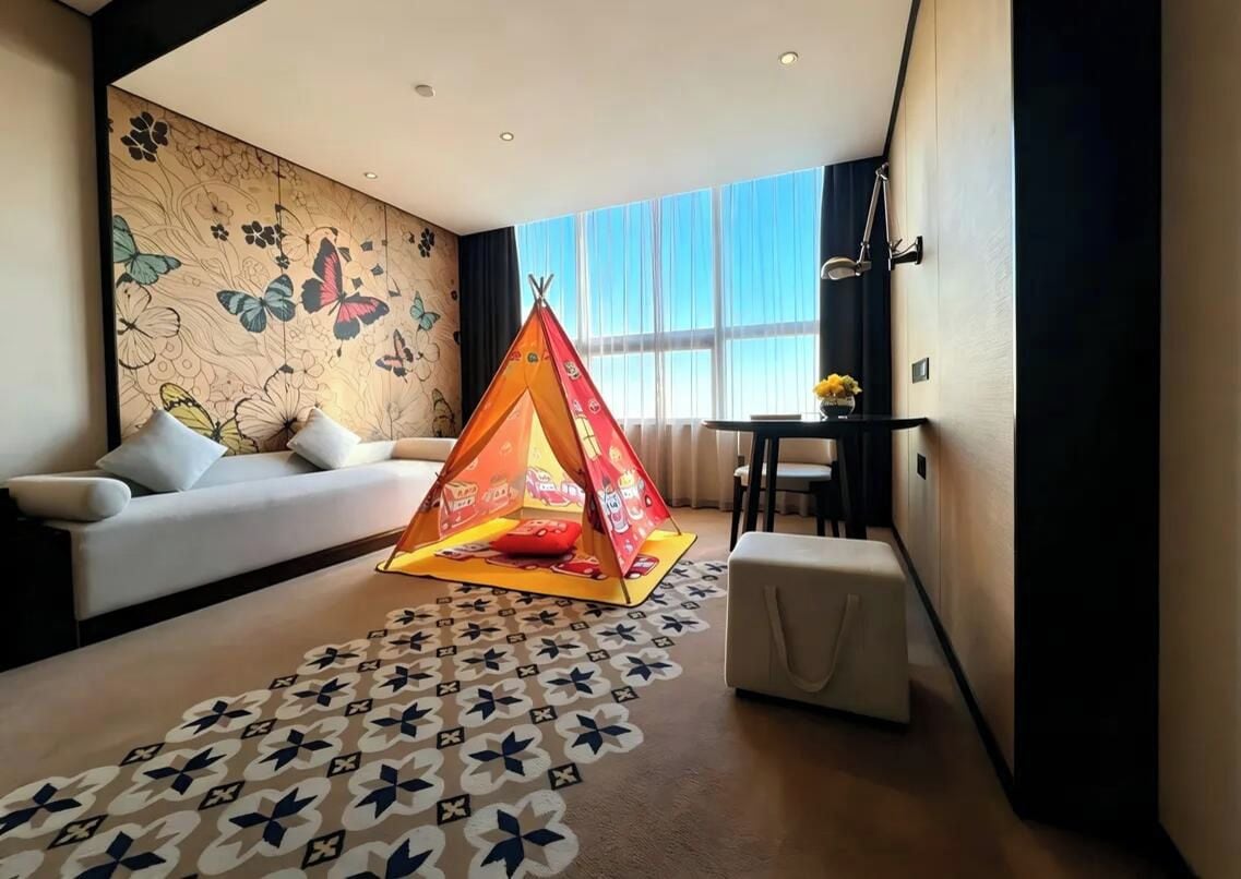 Une chambre d’hôtel avec une grande fenêtre, un canapé, un tapis à motifs et une structure colorée en forme de tente.