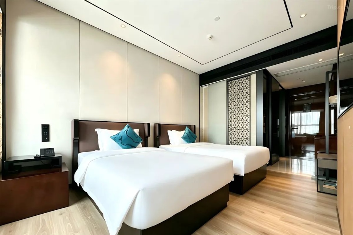 A modern hotel room with two beds, a wooden floor, a nightstand, and a decorative wall panel.