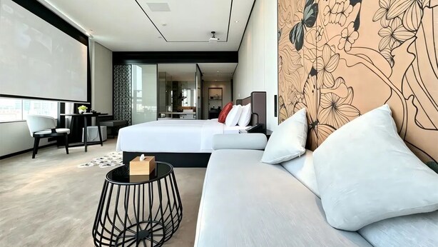 A modern hotel room with a large bed, a sofa, a small round table, and a decorative wall.