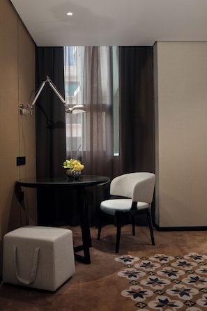 Una habitación moderna con escritorio, silla, reposapiés y un jarrón decorativo con flores.