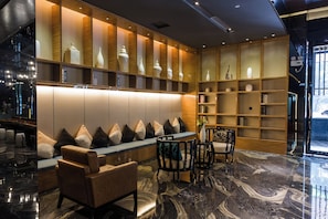 A modern lobby with a seating area, bookshelves, and a marble floor.
