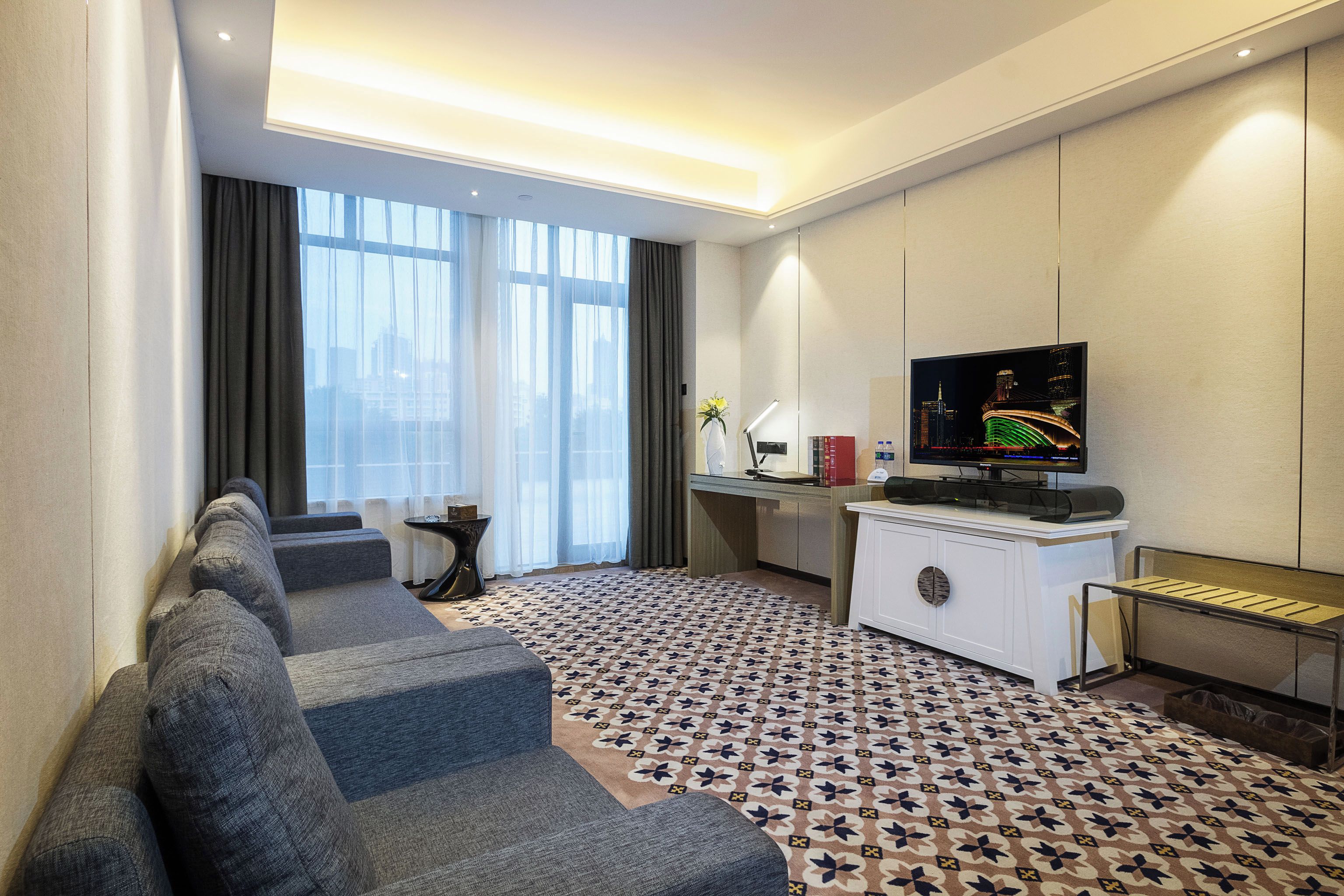 A hotel room with a sofa, a desk, a television, and a patterned carpet.