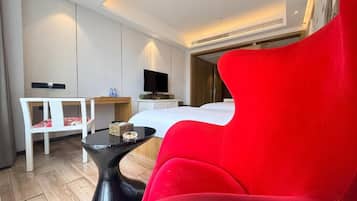 Ein modernes Hotelzimmer mit einem roten Sessel, einem Bett, einem Schreibtisch und einem Fernseher.