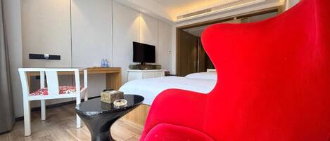 A modern hotel room with a red armchair, a bed, a desk, and a television.