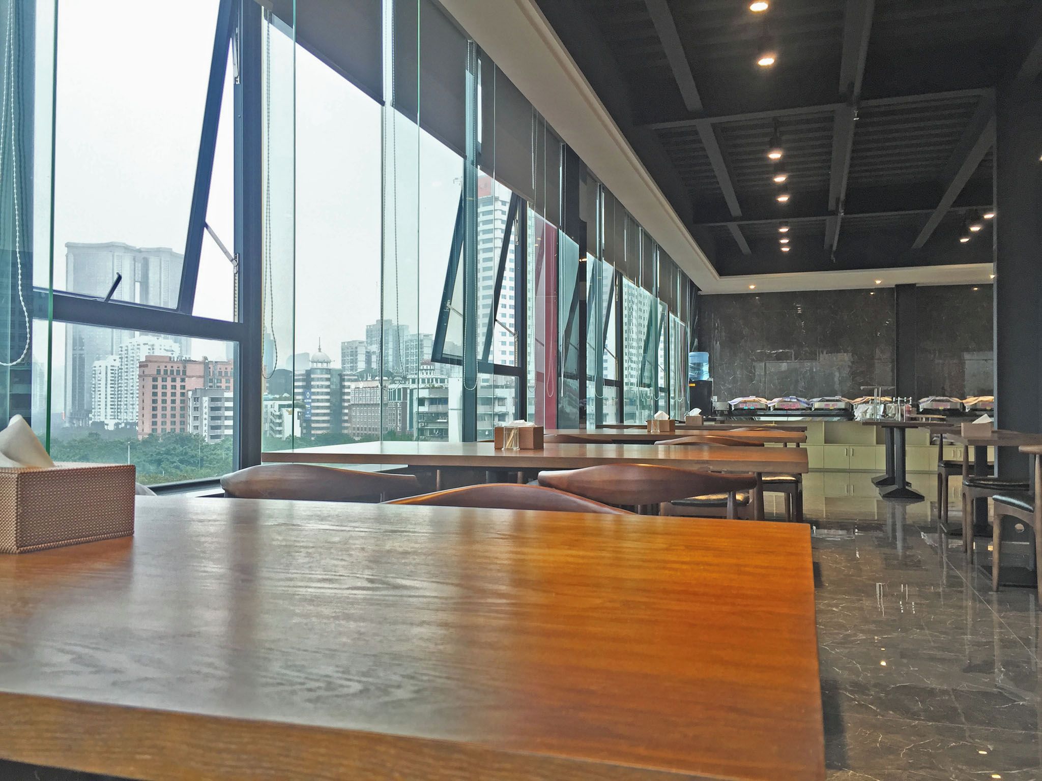 A spacious indoor area with large windows, a long wooden table, and multiple seating arrangements.
