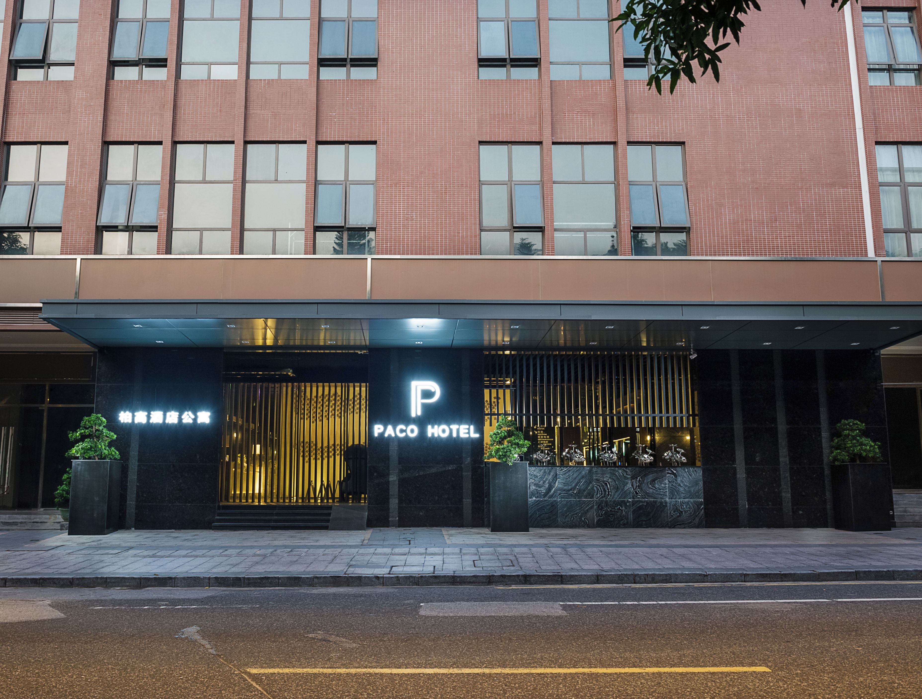 A hotel entrance with a modern facade, a prominent 'Paco Hotel' sign, and a gated entrance.