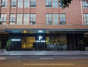 A hotel entrance with a modern facade, a prominent 'Paco Hotel' sign, and a gated entrance.