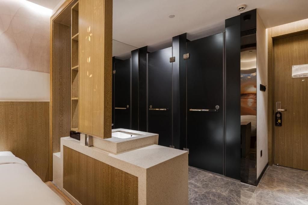 A hotel bathroom with a large mirror, a sink, and a wooden vanity. There are multiple black lockers and a wooden door.
