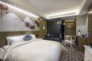 A hotel room with a large bed, a desk, a chair, and a bathroom visible through an open door.