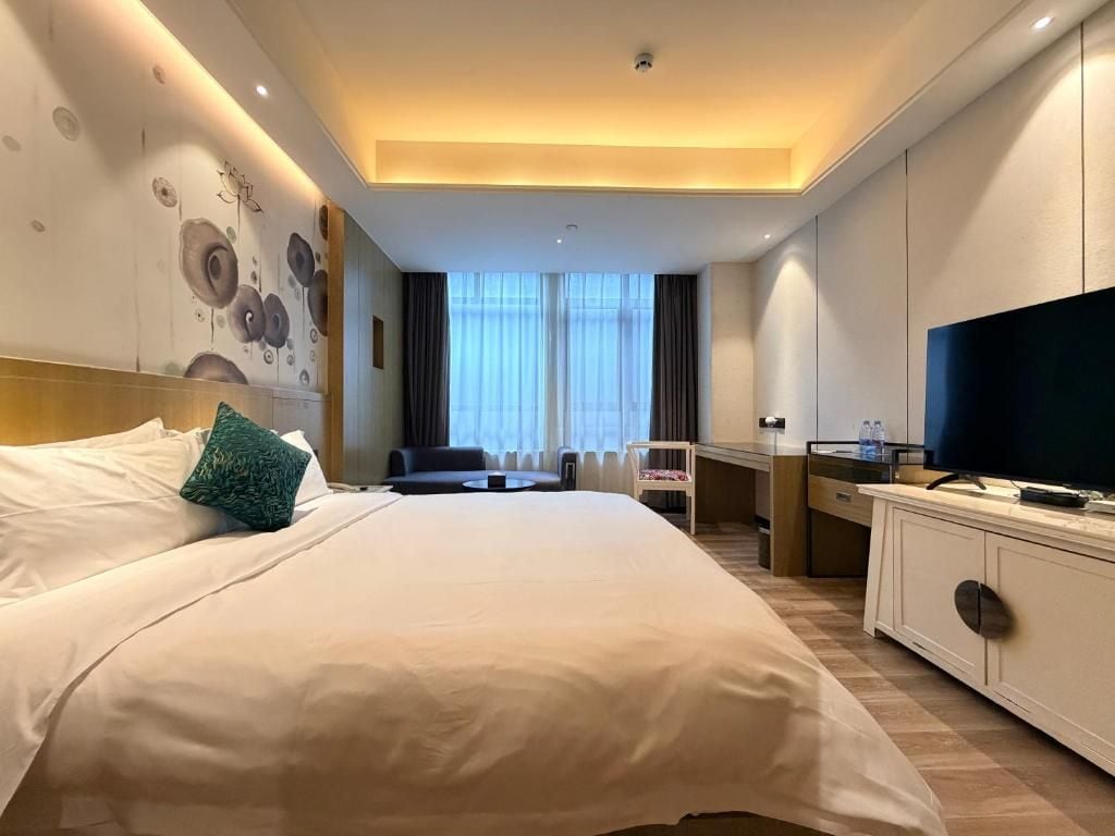 Quarto de hotel com uma cama grande, uma escrivaninha com cadeira, televisão e janela com cortinas.