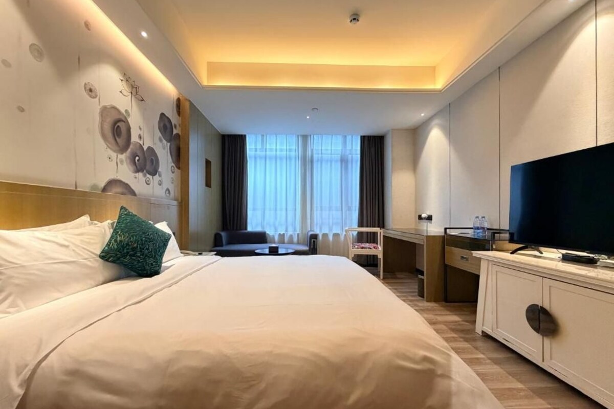 A hotel room with a large bed, a desk with a chair, a television, and a window with curtains.