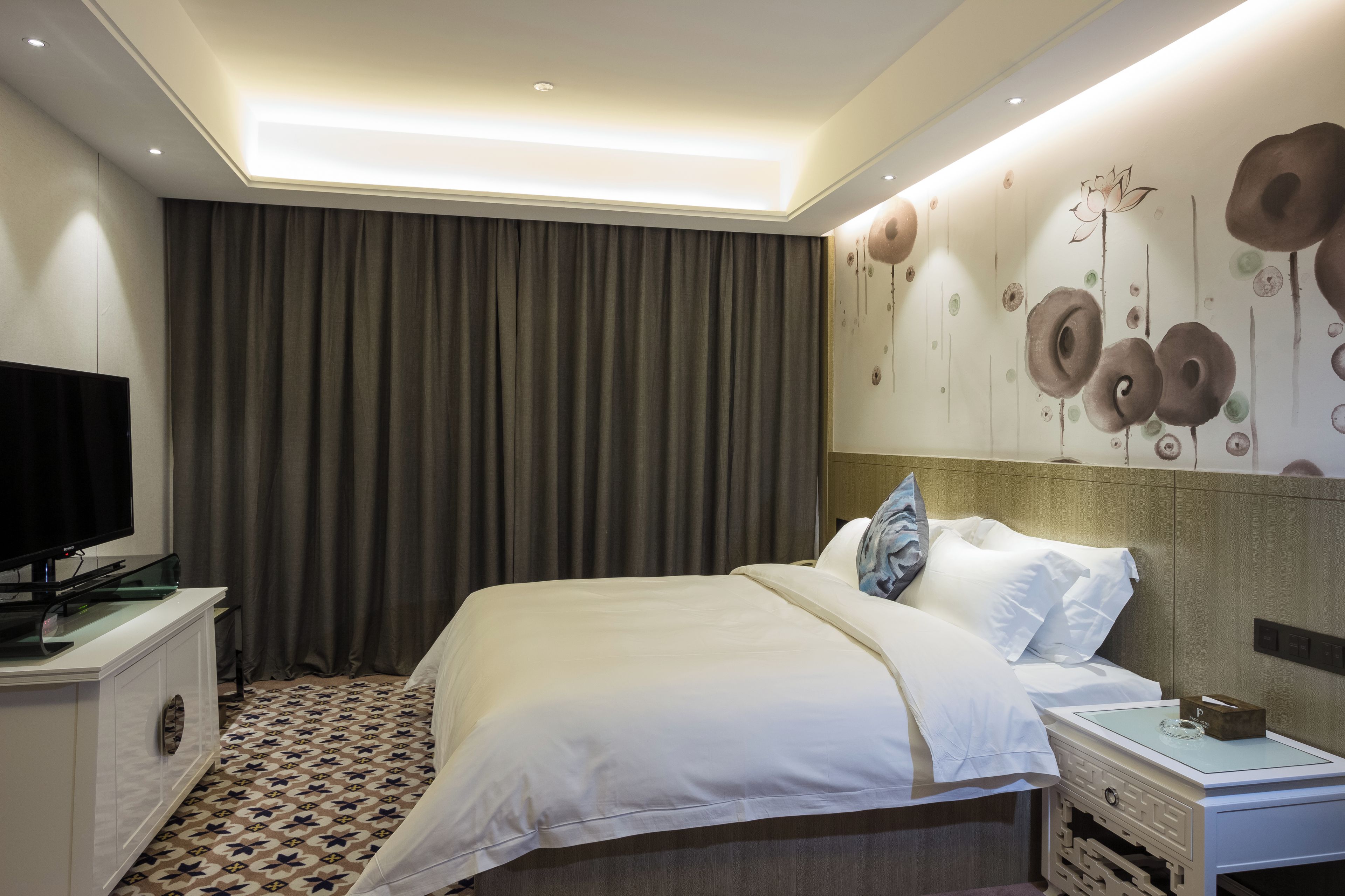 Habitación de hotel con una cama grande, un televisor en un mueble y una pared con diseño circular.