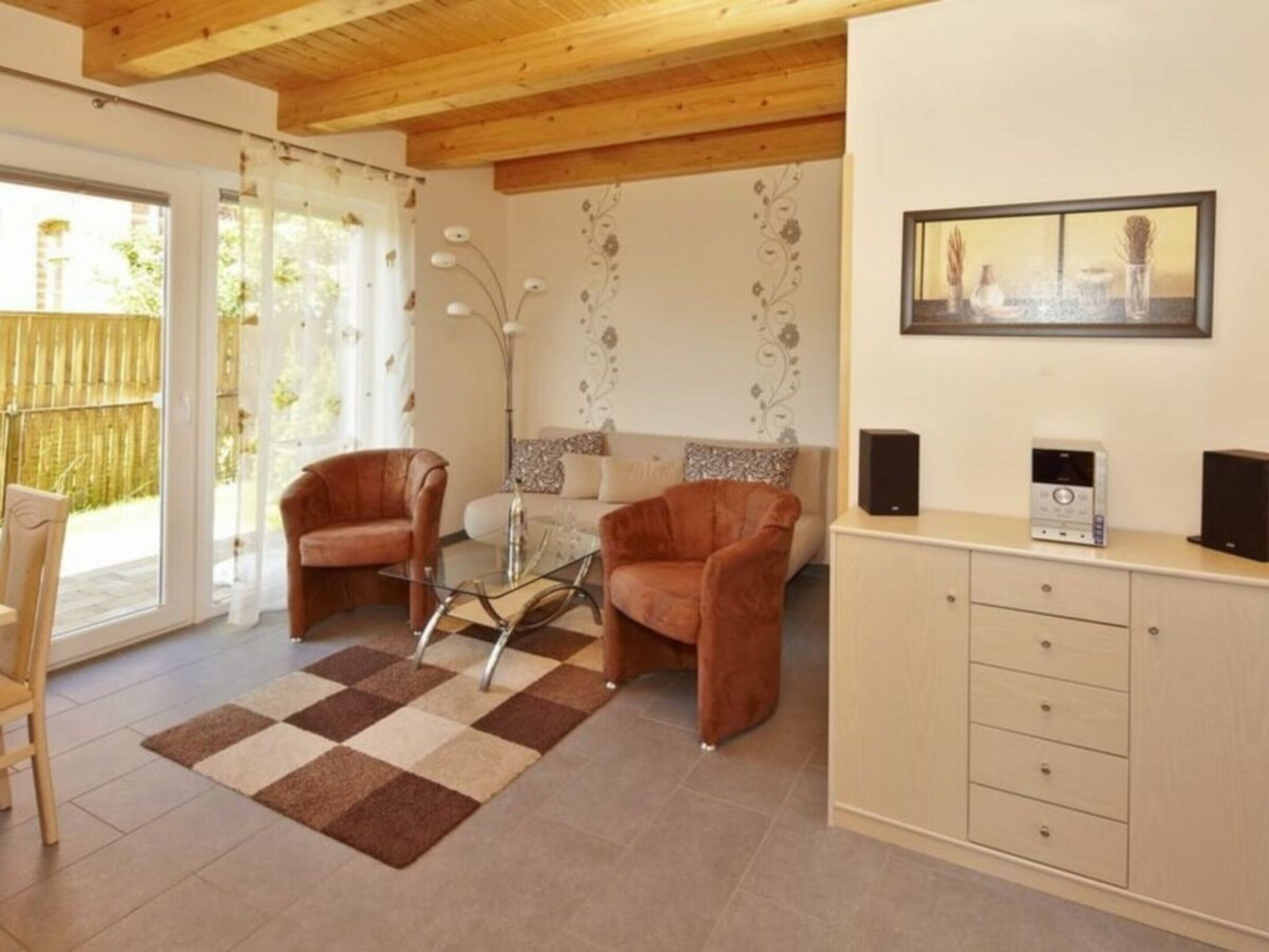 Ein Wohnzimmer mit zwei braunen Ledersesseln, einem Glastisch, einer Couch, einer Wand mit Muster, einem Gemälde und einer Anrichte mit zwei Lautsprechern.
