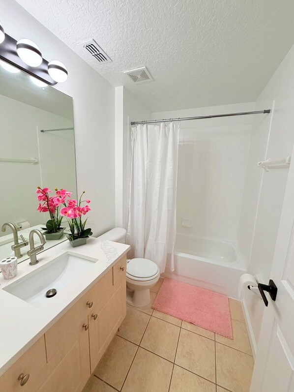 A bathroom with a white sink, mirror, and toilet, a shower curtain, and a pink bath mat. - Disney Family Home/3-bedroom townhome with private pool in Kissimmee. (Kissimmee)