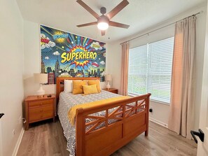 Quarto com cama, ventilador de teto, janela com cortinas e um mural na parede.