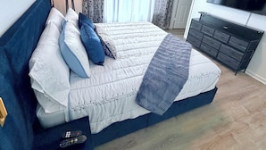 Een slaapkamer met een bed, een televisie, een plafondventilator en een raam met gordijnen.