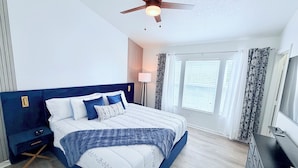Een slaapkamer met een bed, nachtkastje, dressoir, plafondventilator en een raam met jaloezieën.