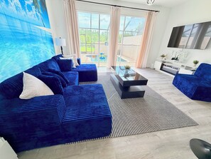 Ein modernes Wohnzimmer mit einem blauen Sofagarnitur, einem Couchtisch und einem an der Wand montierten Fernseher.