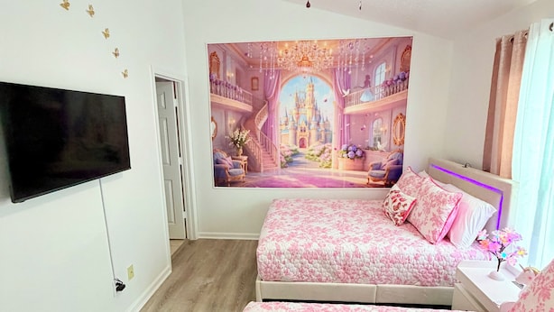 Een slaapkamer met een groot bed, een plafondventilator, een flatscreen-tv en een muurschildering.
