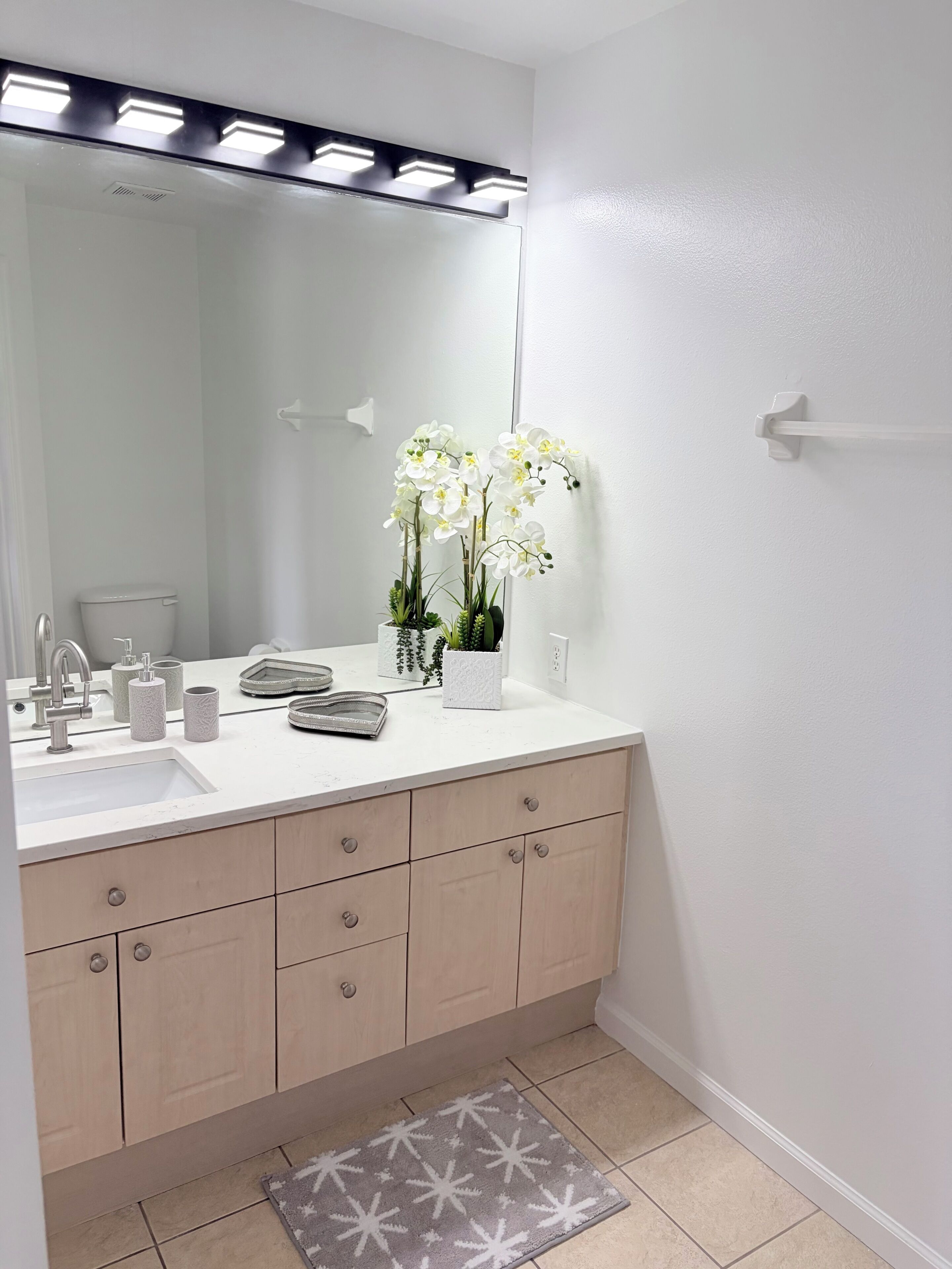 Une salle de bain avec un lavabo blanc, un miroir et une orchidée en pot.