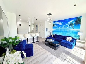 Uma sala de estar moderna com um sofá azul, uma mesa de centro e um grande mural tropical na parede.