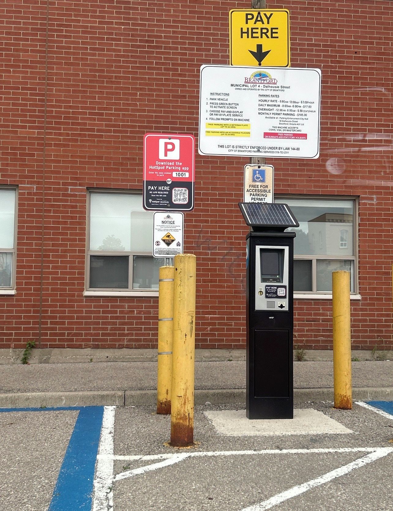 A parking meter and payment kiosk in front of a brick building with a parking sign.