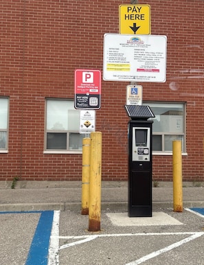 A parking meter and payment kiosk in front of a brick building with a parking sign.