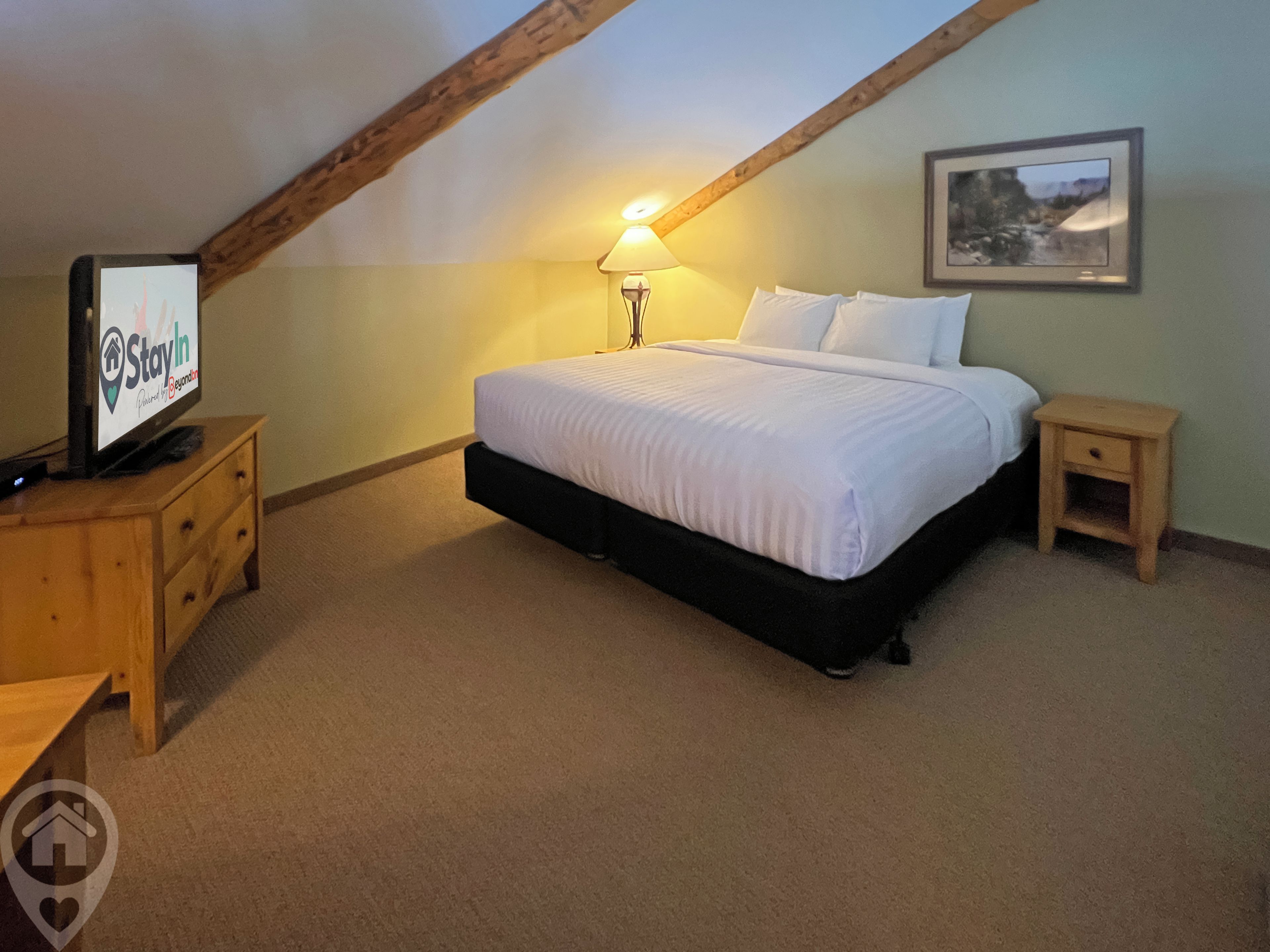 A bedroom with a bed, a nightstand, a lamp, a TV, and a framed picture on the wall.