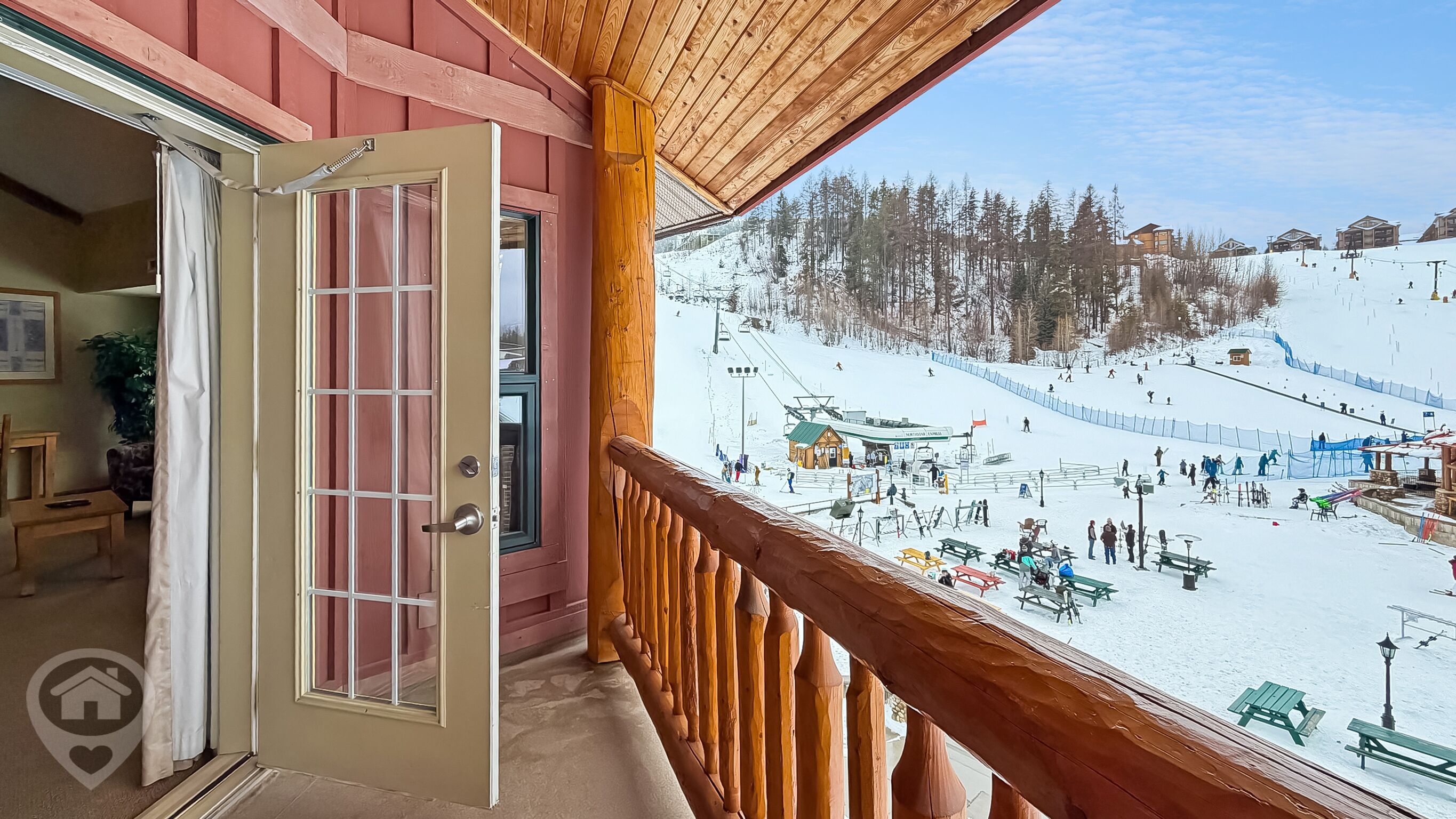 Un balcon en bois offrant une vue sur une piste de ski enneigée et un chalet.