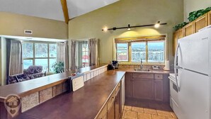 A kitchen with a long counter, a sink, and a refrigerator. There are windows with curtains, and a view of buildings outside.