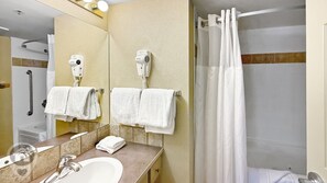 Un bagno con lavandino, specchio, portasciugamani e doccia con tenda.