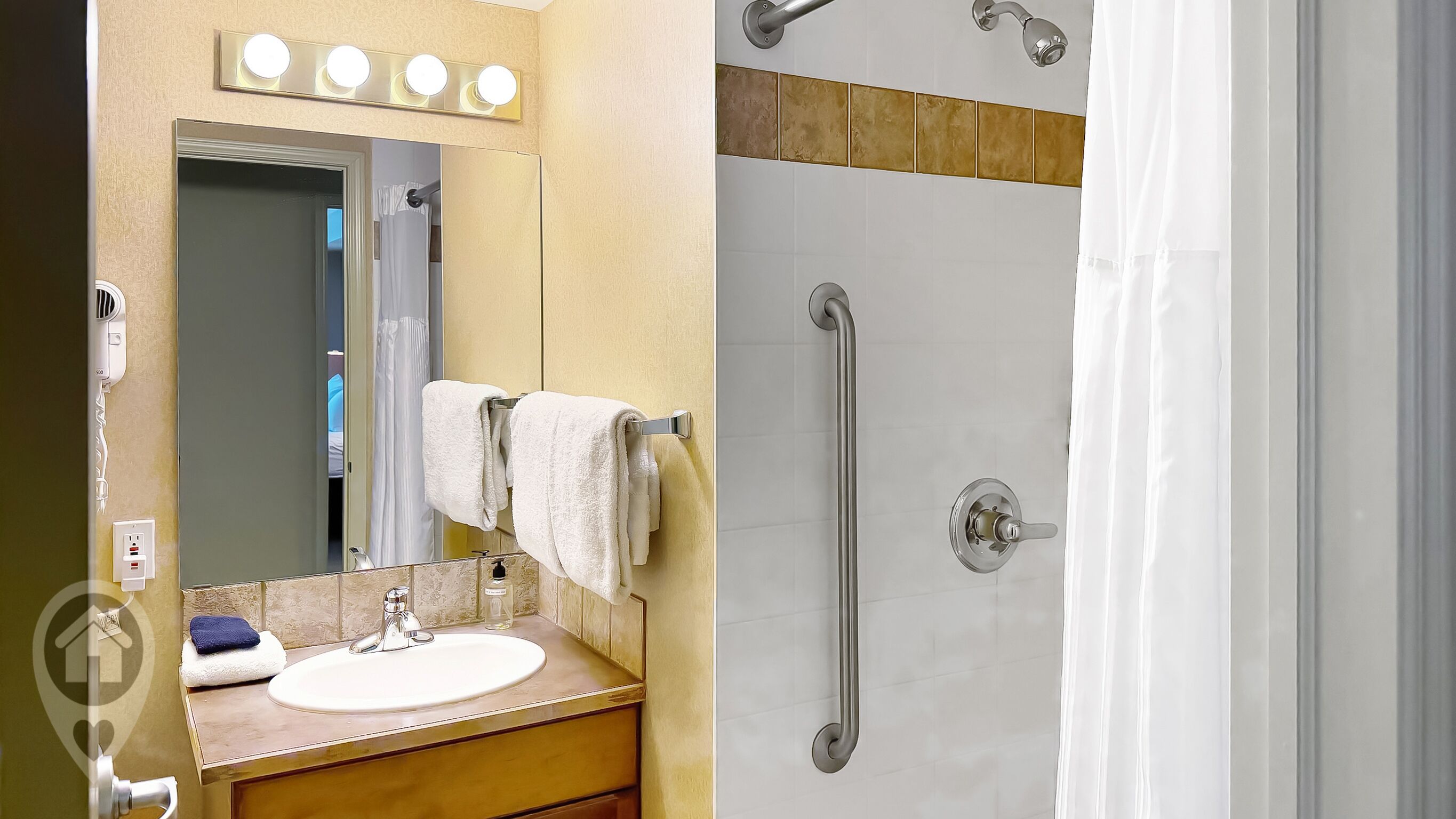 A bathroom with a sink, mirror, and a shower with a grab bar.