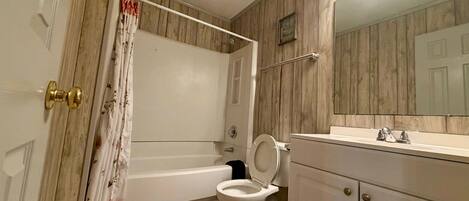 A bathroom with a bathtub, toilet, and vanity with a mirror.