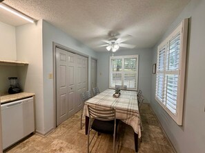 A compact kitchen with a dining area, a ceiling fan, and a window with blinds.
