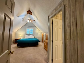 A bedroom with a sloped ceiling, a bed, a dresser, and a window.