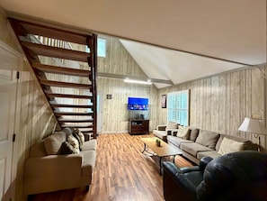 A living room with a wooden floor, a staircase, a flat-screen TV, and two sofas. - Duke Medical District Stay House FenceYard (Durham)