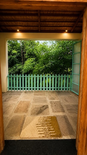 A covered outdoor area with a stone floor, a green fence, and a view of trees.