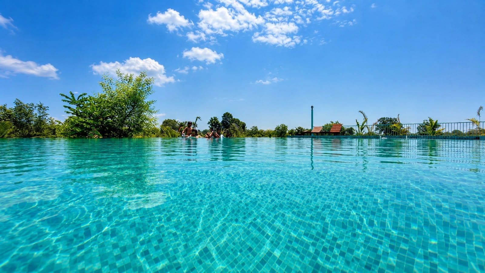 A clear blue pool surrounded by lush greenery and a clear sky.