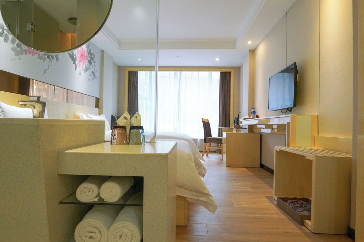 A hotel room with a bed, a desk, a television, a mirror, and a shelf with towels.
