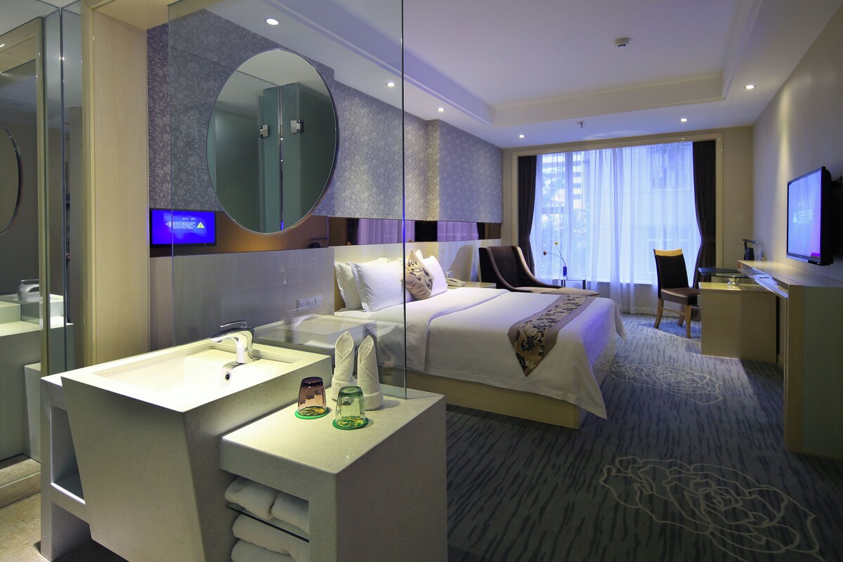 A hotel room with a bed, a desk, a television, and a bathroom with a mirror and sink.