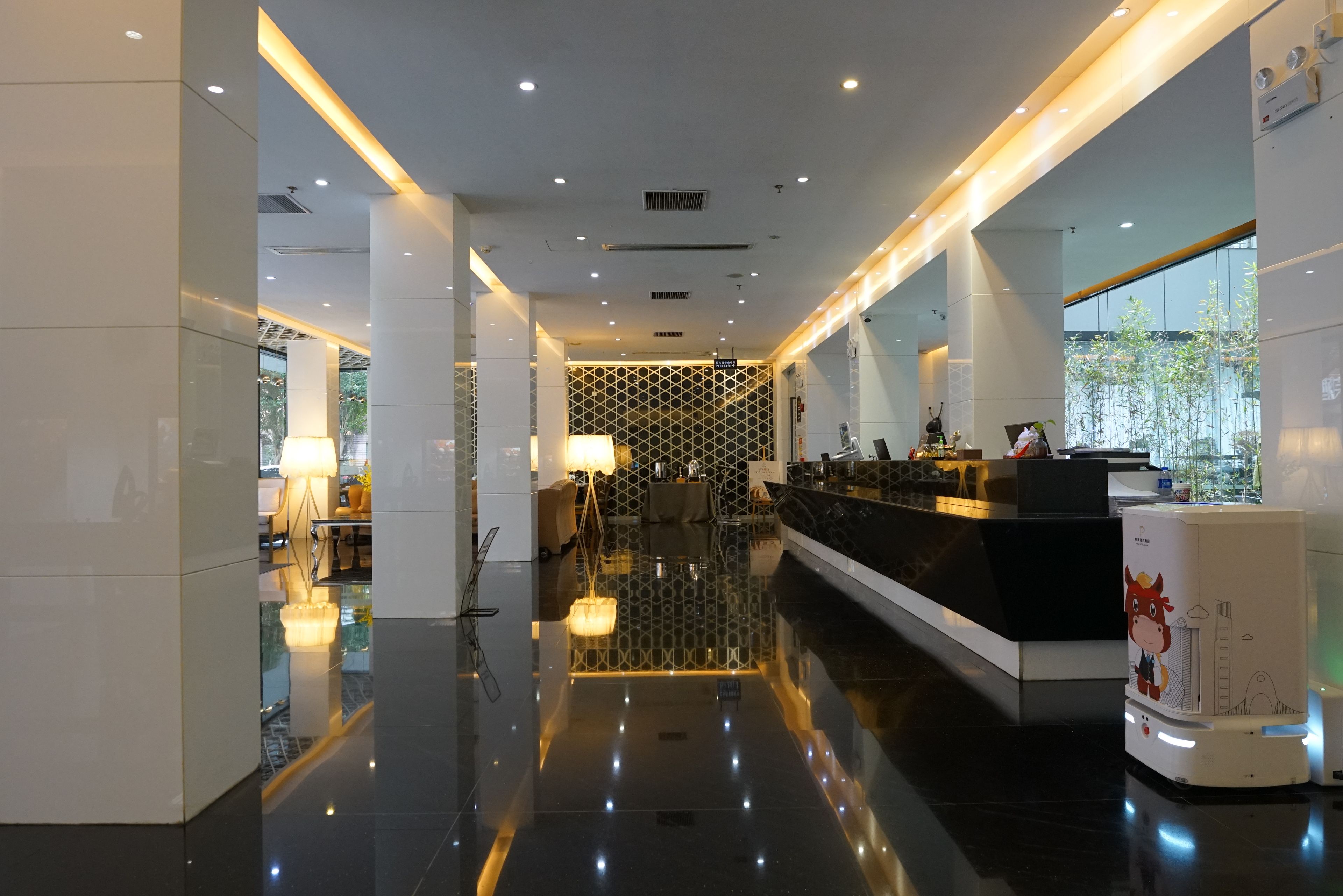 A modern hotel lobby with a reception desk, seating area, and a glass partition wall.