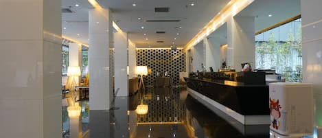 Un moderno vestíbulo de hotel con mostrador de recepción, zona de estar y un muro divisorio de vidrio.