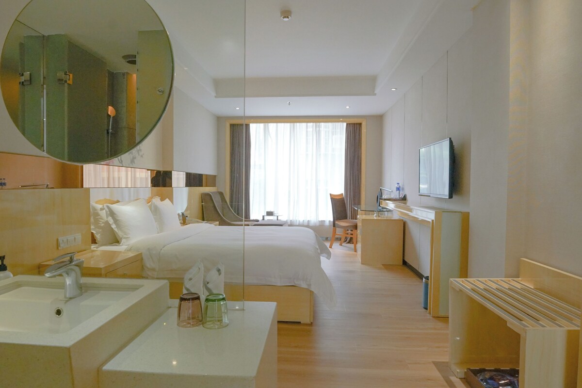 A hotel room with a bed, a desk, a television, and a large mirror.