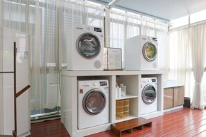 A laundry room with multiple washing machines, a wooden bench, and a glass door leading outside. - Paco Hotel Ouzhuang Metro Guangzhou (Guangzhou)