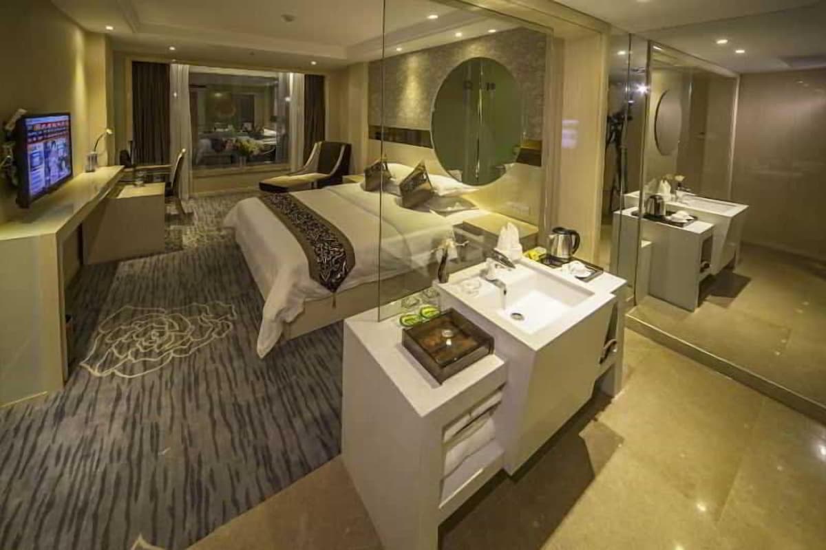 Quarto de hotel moderno com uma cama grande, uma escrivaninha com computador, um banheiro com espelho e vista para a cidade.