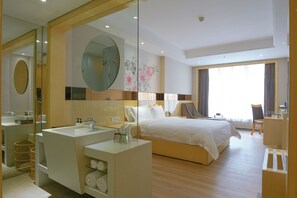 A hotel room with a large bed, a sitting area with a chair, a desk, a bathroom with a mirror, and a large window. - Paco Hotel Ouzhuang Metro Guangzhou (Guangzhou)