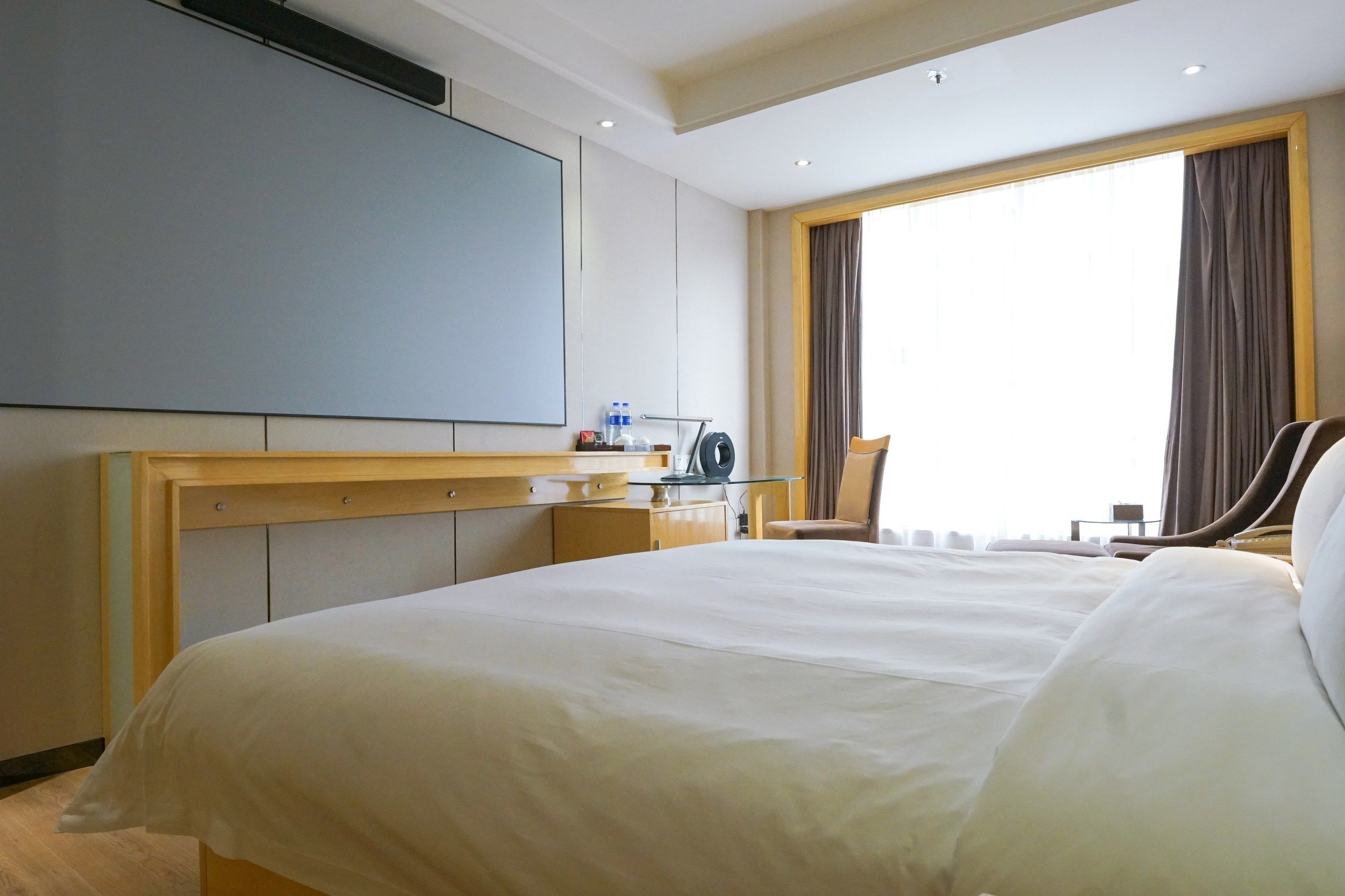 Quarto de hotel com uma cama grande, escrivaninha com cadeira, televisão de tela plana e janela com cortinas.