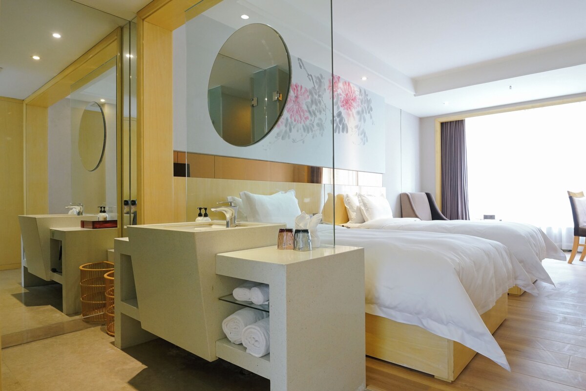 A hotel room with a large bed, a separate bathroom with a mirror, and a view of the outdoors.