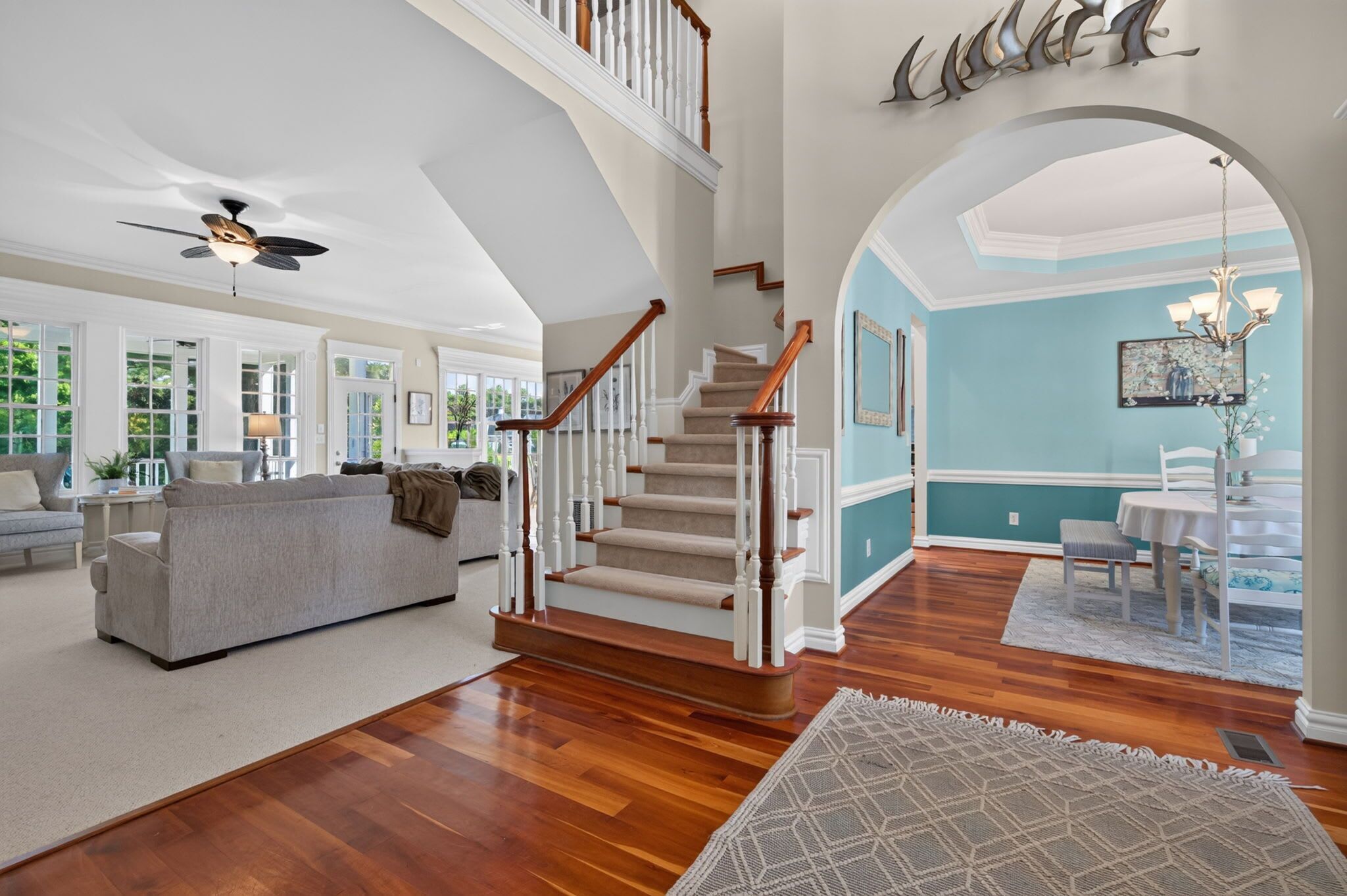 A spacious living room with a staircase, a dining area, and a view through an archway.