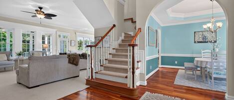 A spacious living room with a staircase, a dining area, and a view through an archway.